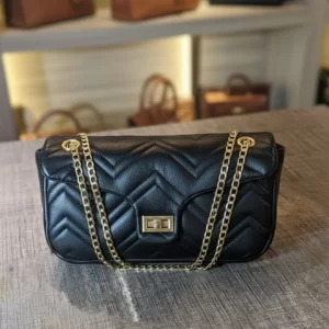 Black quilted crossbody bag with gold chain strap displayed on table – front view