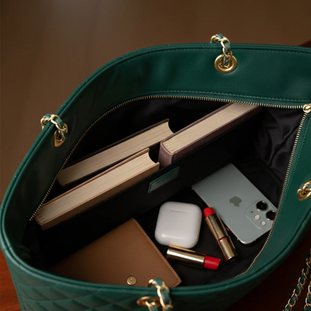 Inner view of deep green quilted tote bag showing black fabric lining with open pocket and zipper pocket