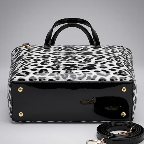 Bottom view of the Vibe Totes white snow leopard ladies bag, displaying a solid black patent base with four gold protective metal feet.